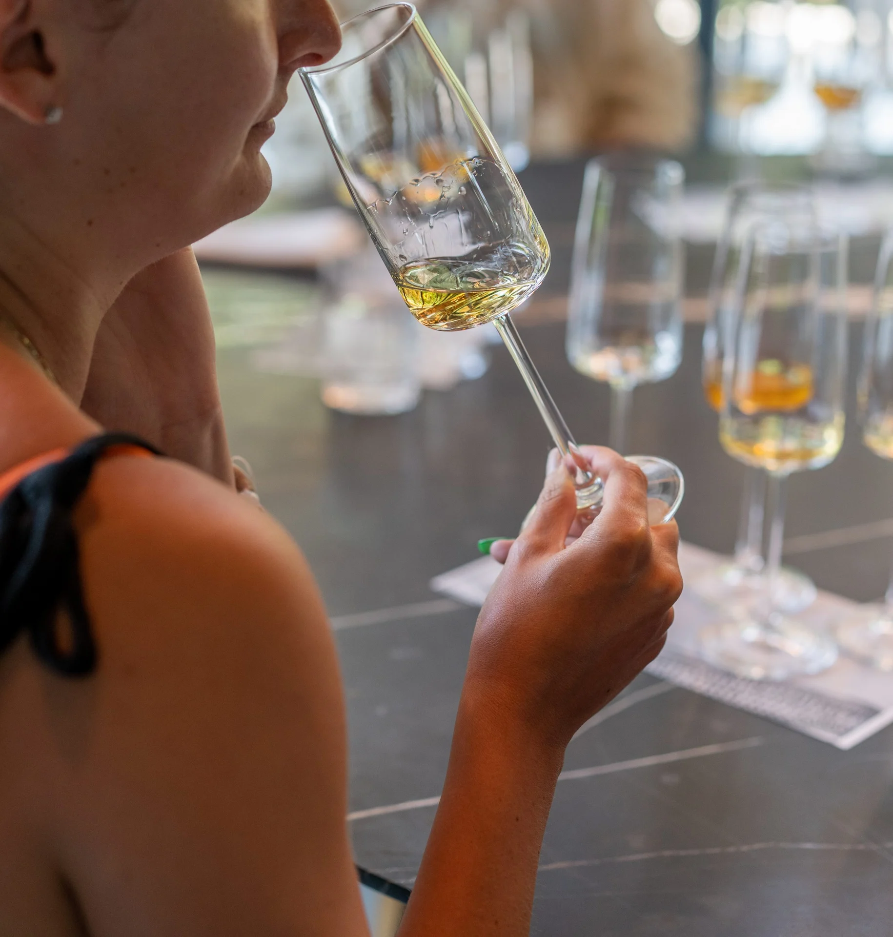 Guest evaluates aroma of amber spirit during a tasting, surrounded by glasses in a modern setting.
