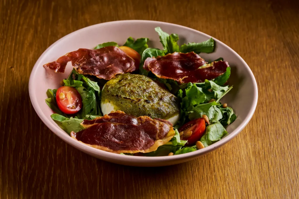 Gourmet burrata salad at Conrad Tulum Riviera Maya, with prosciutto, cherry tomatoes, pine nuts, and pesto.