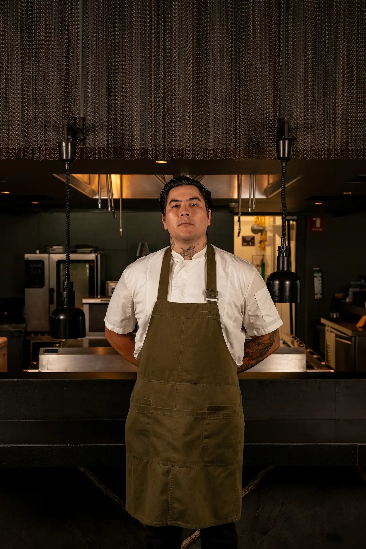 Chef Dante Osmani in white coat and green apron standing in the professional kitchen of Autor Restaurant.