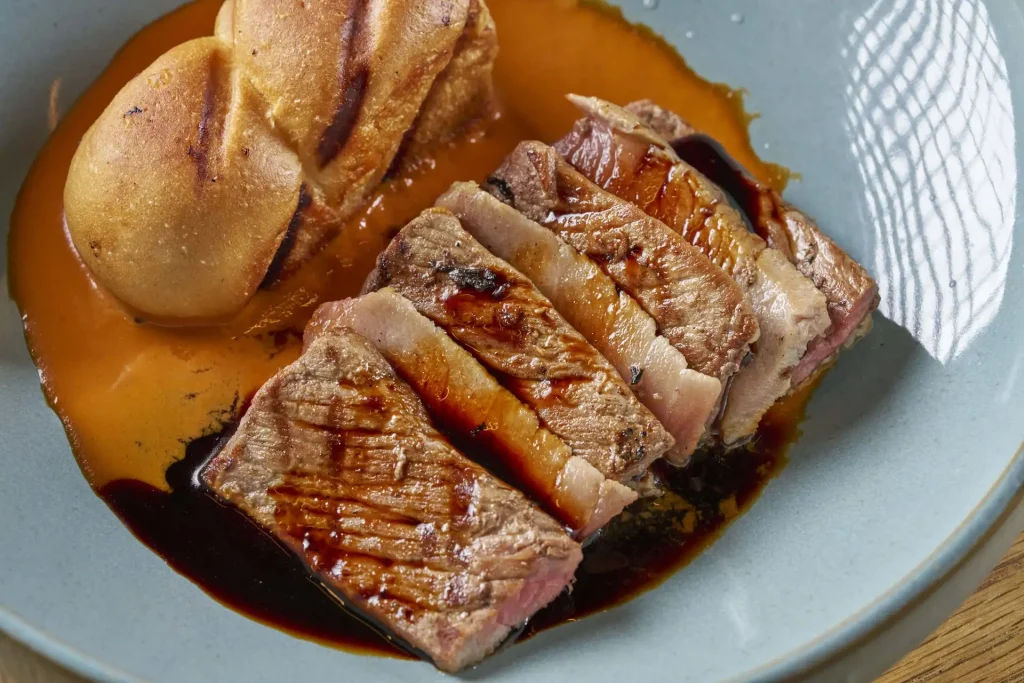 Sliced grilled steak with dark glaze served with grilled bread and orange sauce at Ukai.