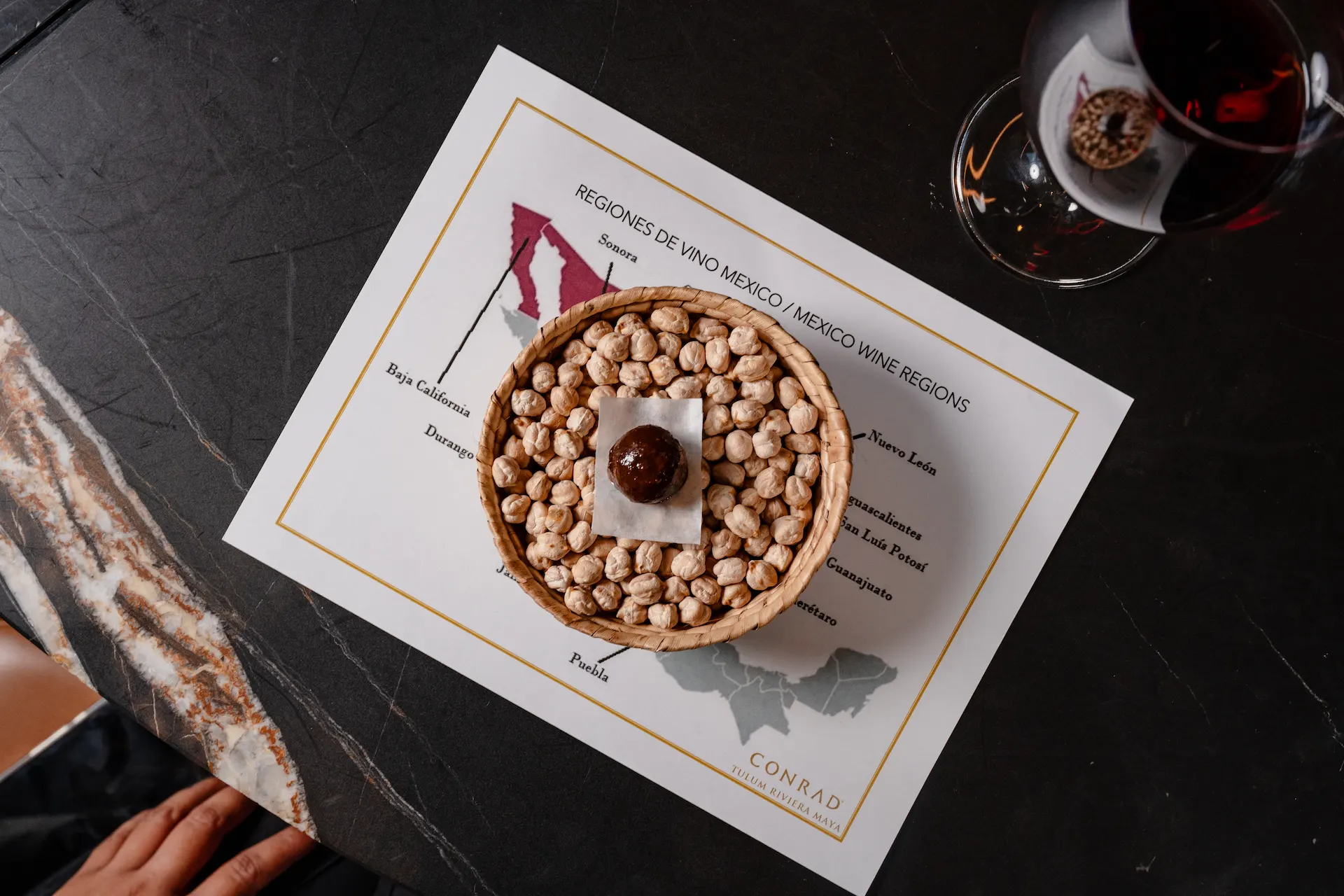 Wicker basket of chickpeas and chocolate truffle atop a Mexico wine region map, with red wine nearby.