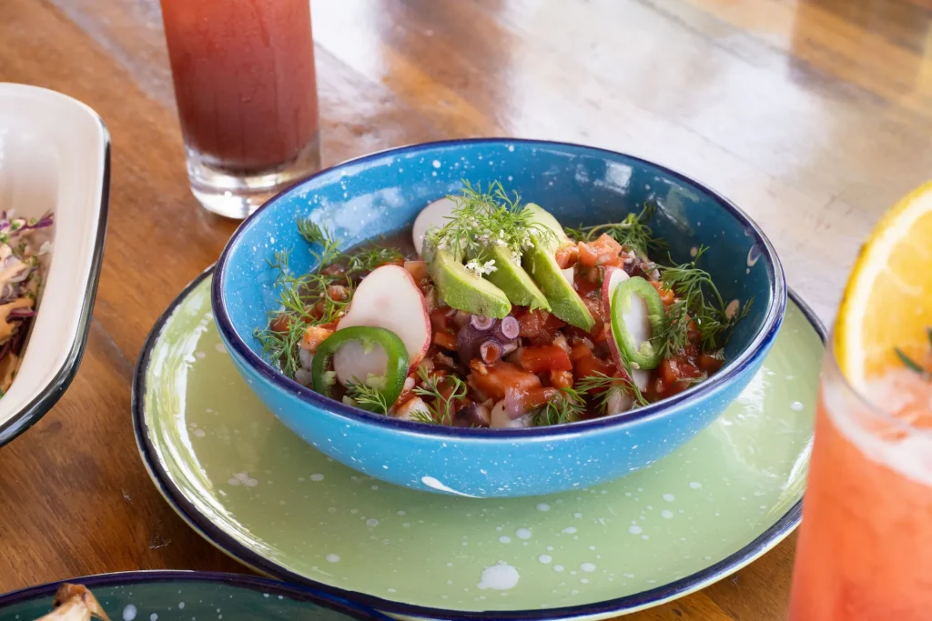 Fresh ceviche with avocado, radish, jalapeño, and dill at CHIRINGUITOS, served in a blue bowl on green plate.