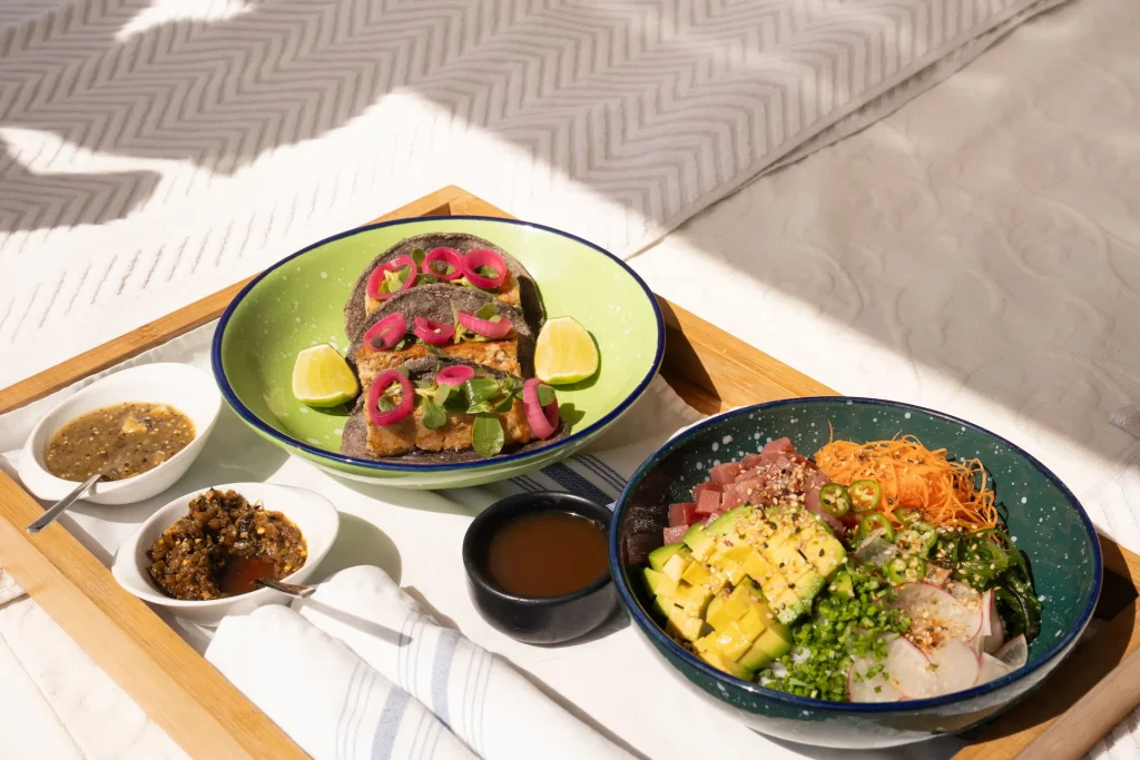 Tray of tacos and poke bowl at ULTRAMAR, with colorful sauces and fresh garnishes on a white table.
