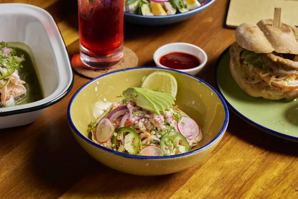 Mexican-inspired dishes at CHIRINGUITOS, including fresh salad, crusty sandwich, seafood plate, and red drink.