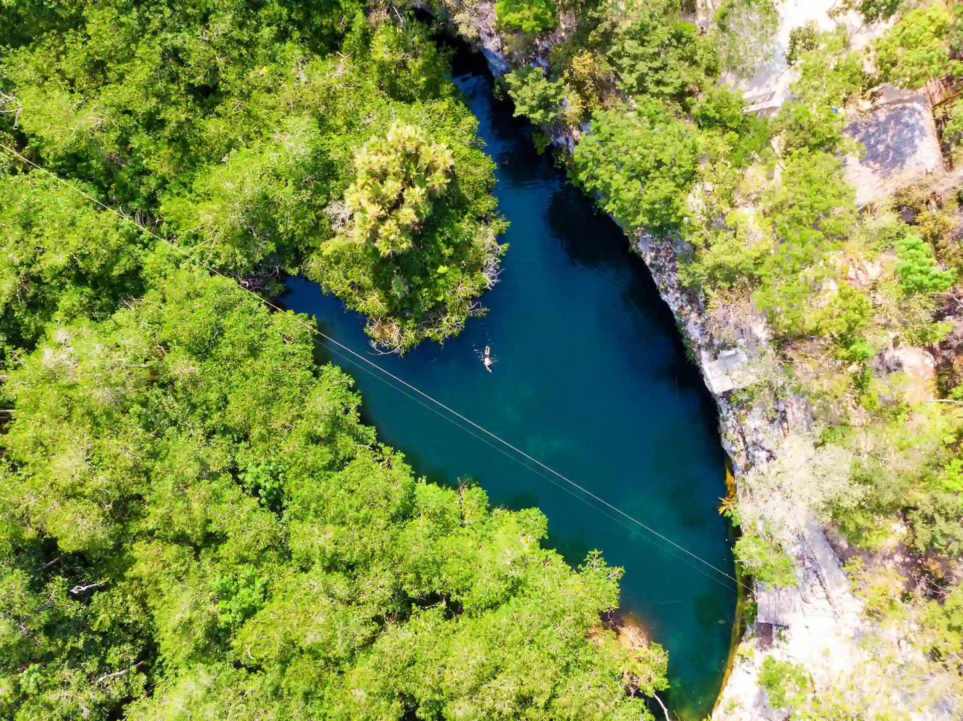 People diving in a cenote in Tulum, surrounded by clear water and natural rock formations.