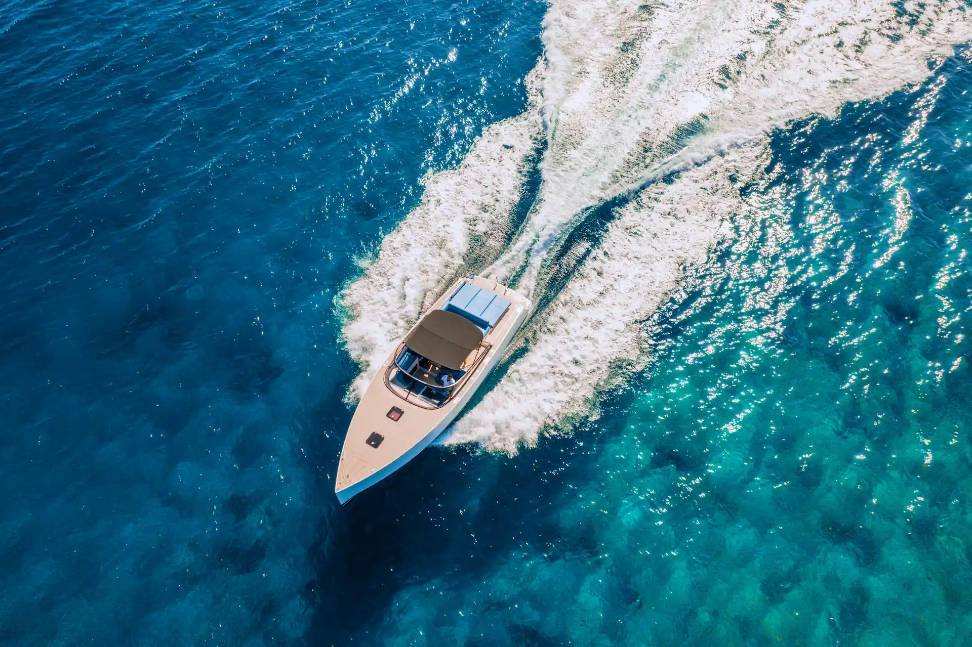 Motorboat speeding through clear blue ocean with white wake and sleek design seen from above