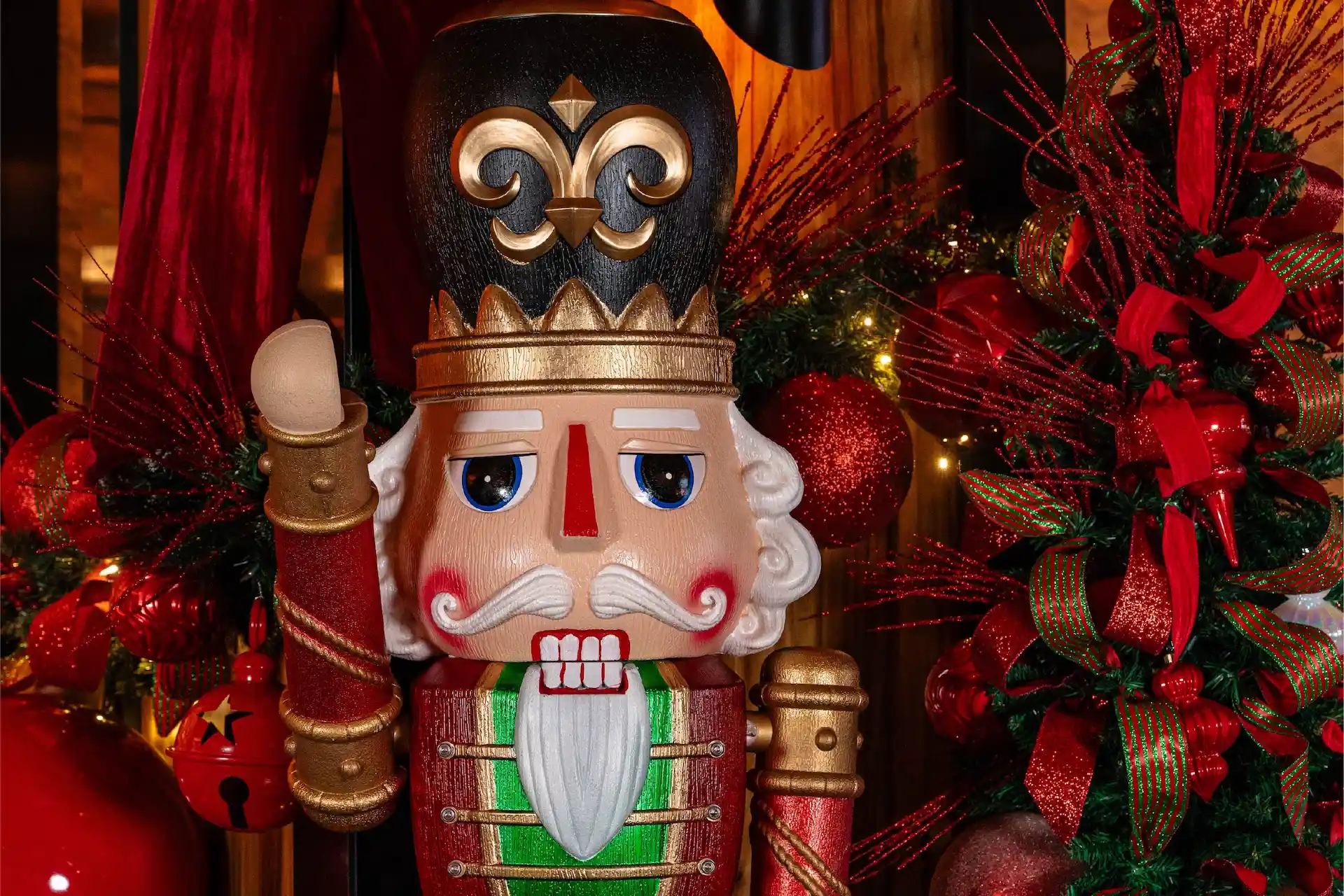 Nutcracker figure with fleur-de-lis hat surrounded by red ornaments, ribbons, and festive greenery
