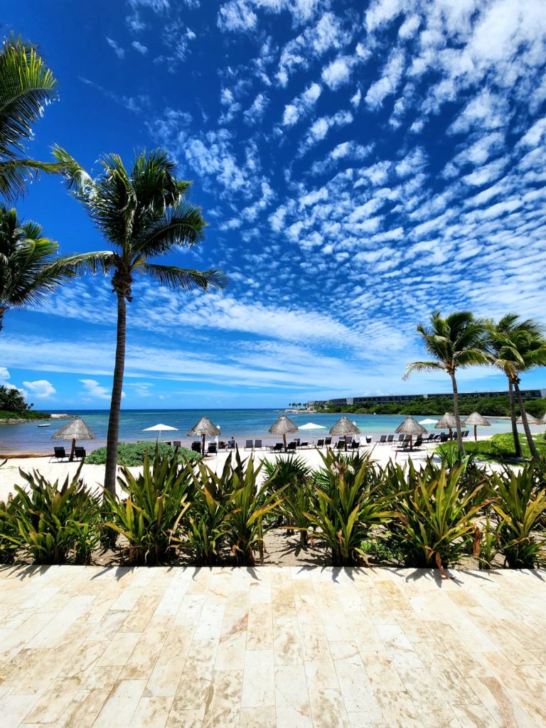 Beachfront at Conrad Tulum Riviera Maya, lounge chairs and palapa umbrellas on white sand with palm trees & turquoise ocean.