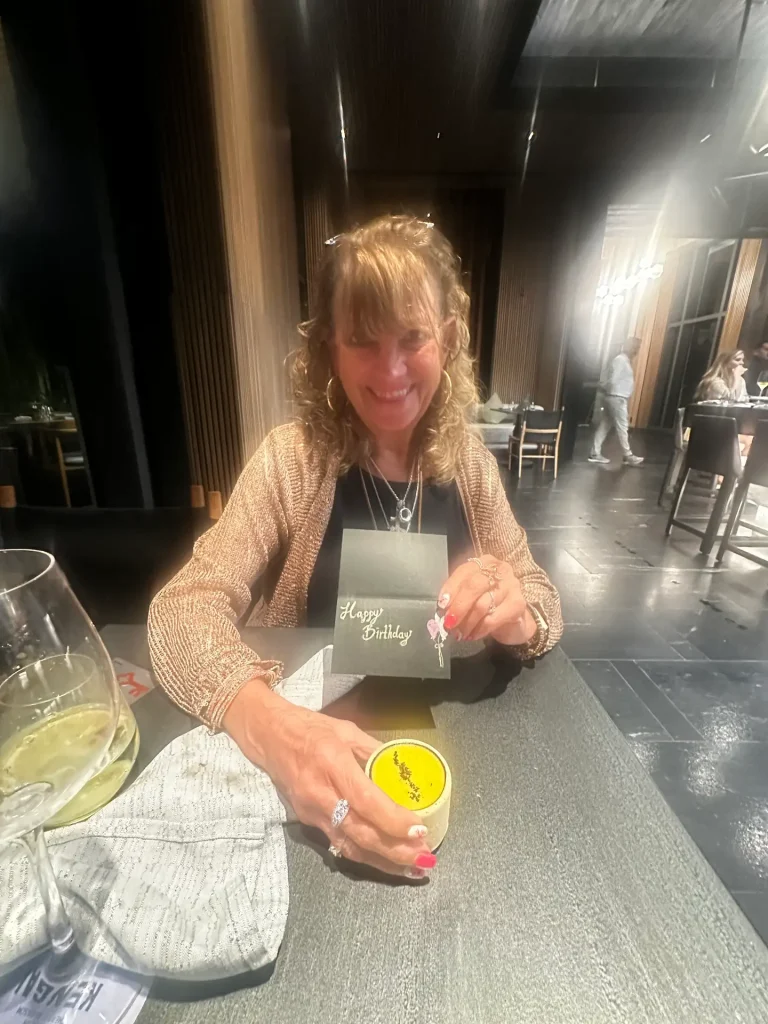 Woman celebrating her birthday at a stylish restaurant, smiling with dessert and greeting card in hand.