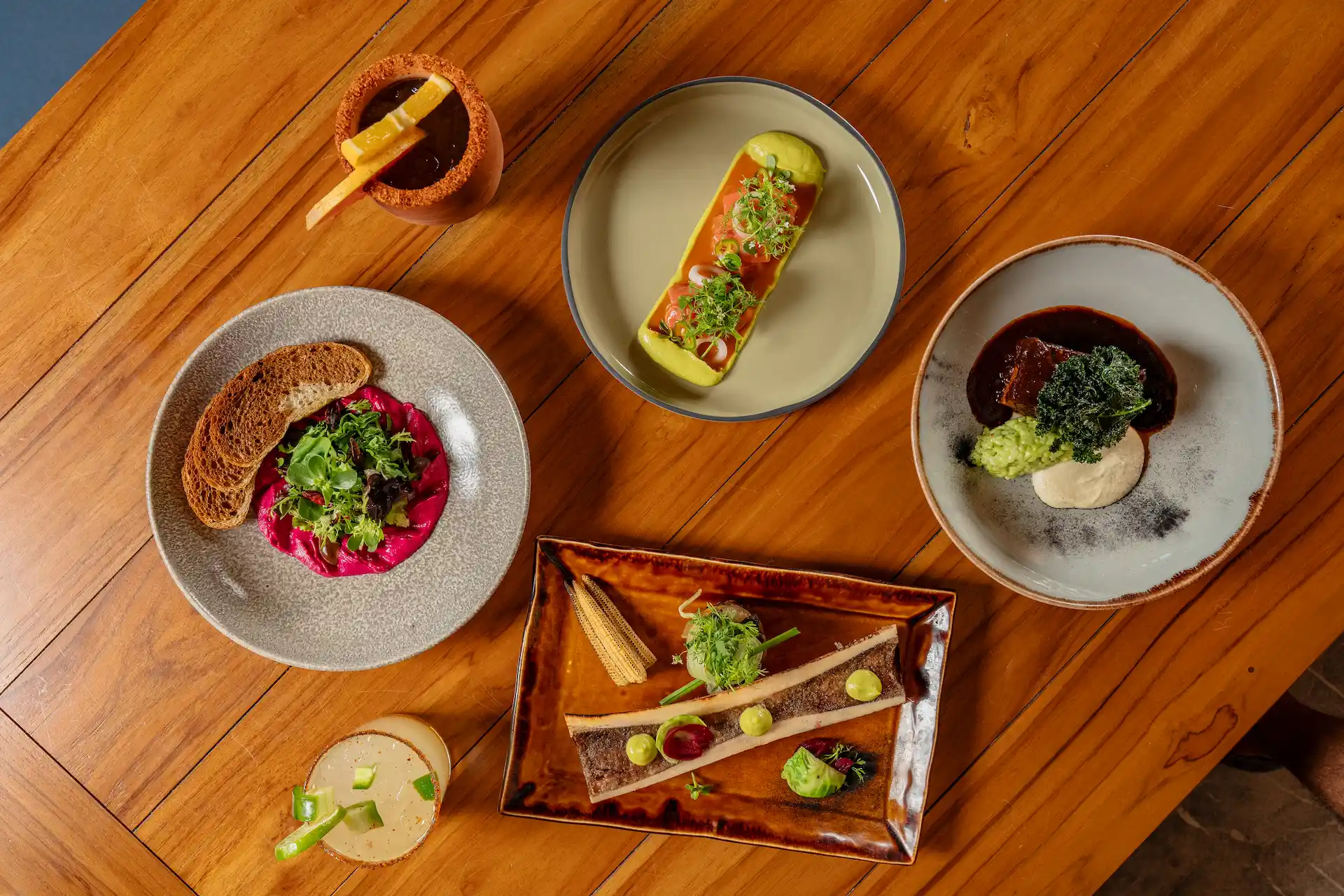 Assorted gourmet dishes and drinks arranged on wooden table with vibrant colors and artistic plating