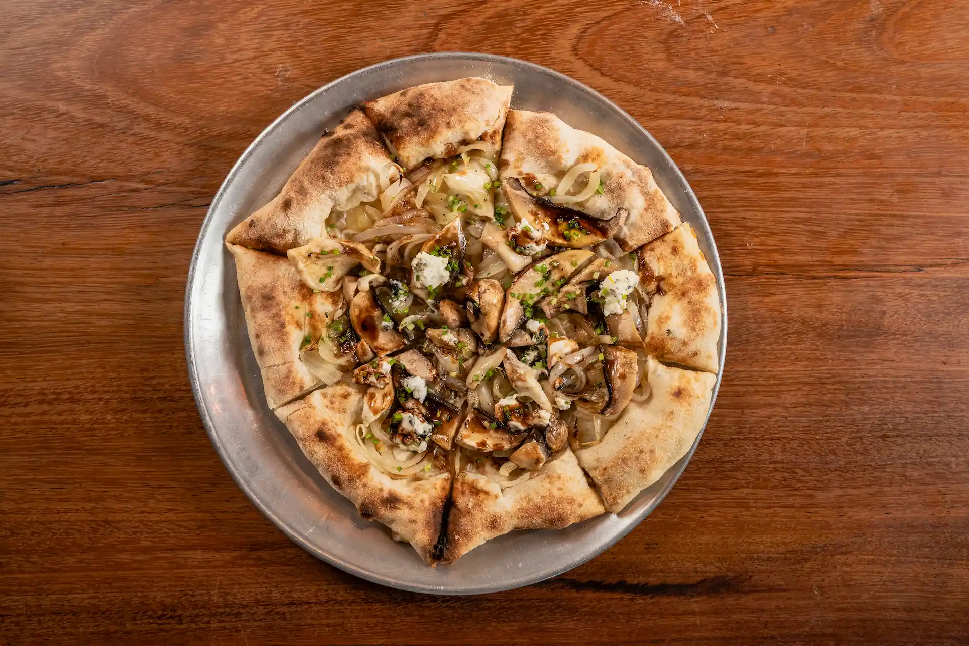 Gourmet pizza with ricotta, mushrooms, caramelized onions, and herbs on metal tray over wood surface