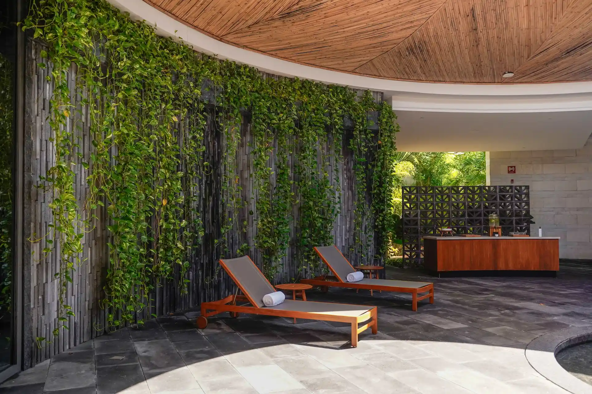 Spa lounge with cushioned wooden chairs, vertical garden wall, and geometric partition in tranquil setting