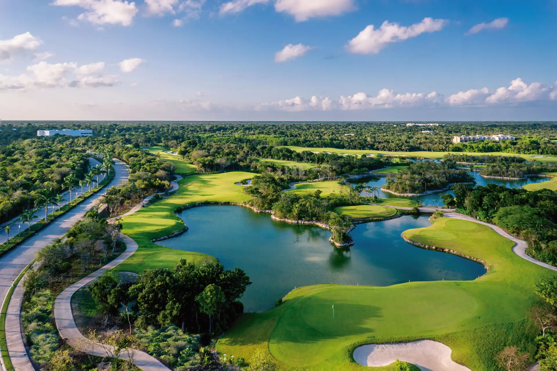 Aerial view of lush golf course in Riviera Maya, with winding paths, water hazards, and tropical forest surroundings.