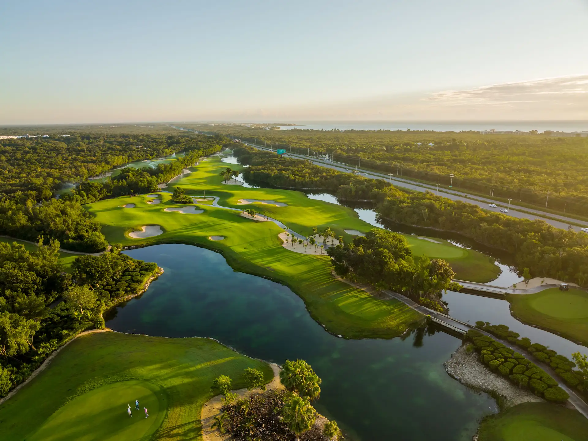 Aerial view of lush golf course with winding fairways, water features, and tropical forest surroundings.