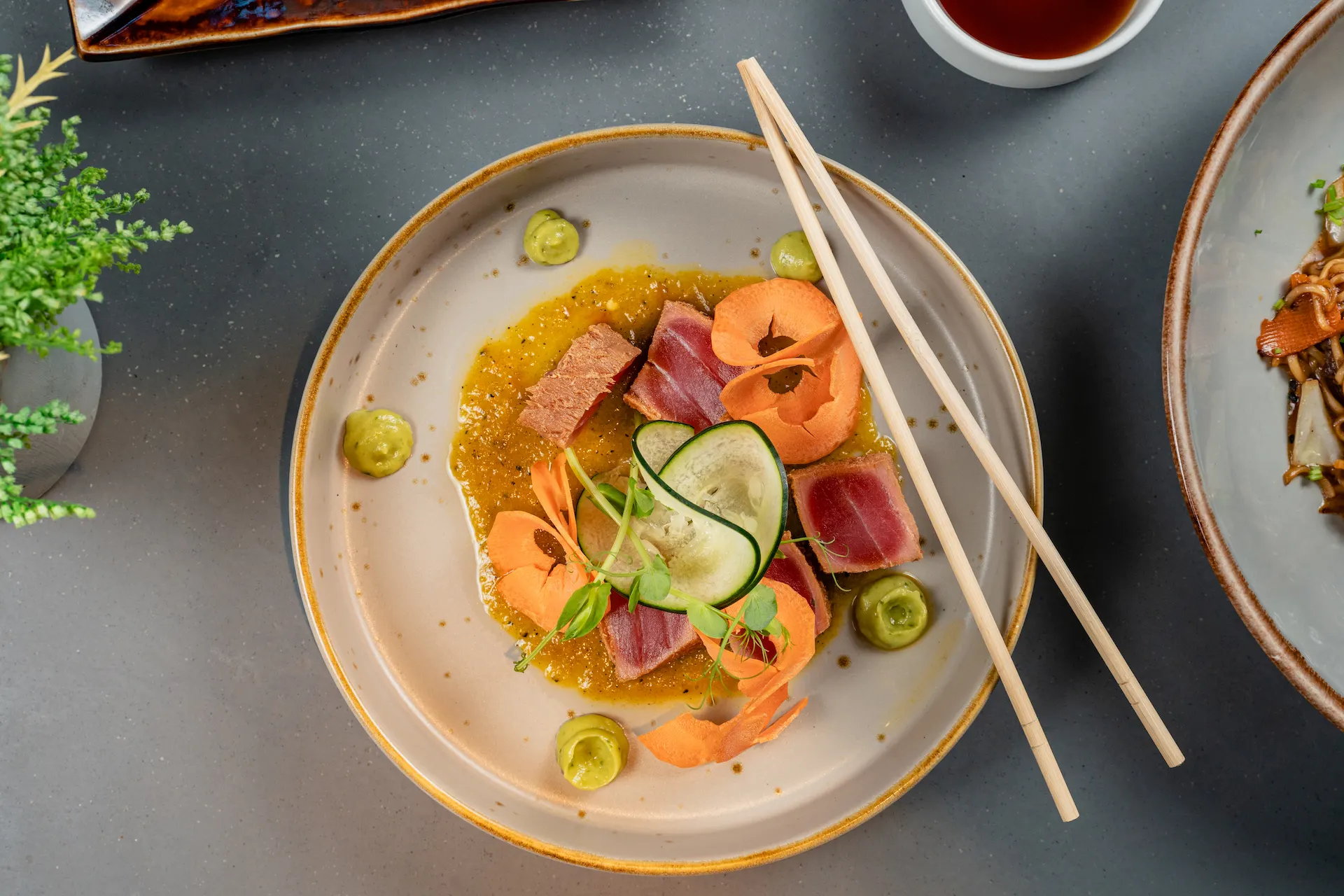 Seared tuna sashimi with cucumber, carrot ribbons, microgreens, and green puree on a ceramic plate.