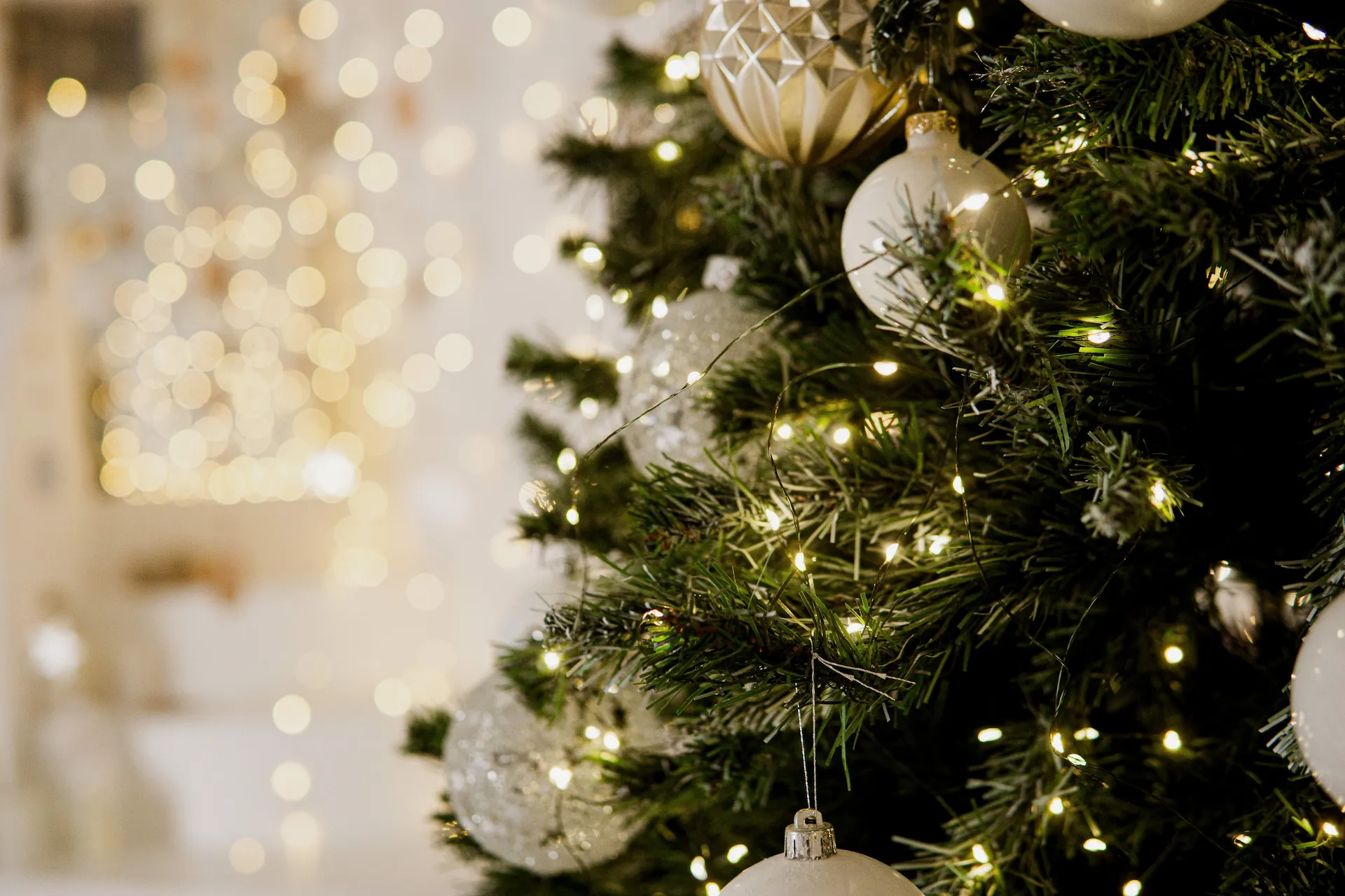 Christmas tree adorned with white, gold, and clear ornaments, glowing with warm lights in a festive setting.